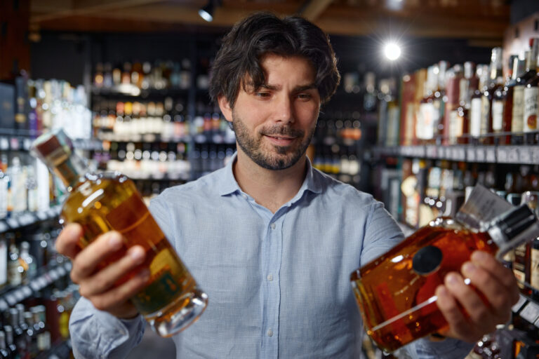 image of A man holds two bottles of alcohol in a liquor store
